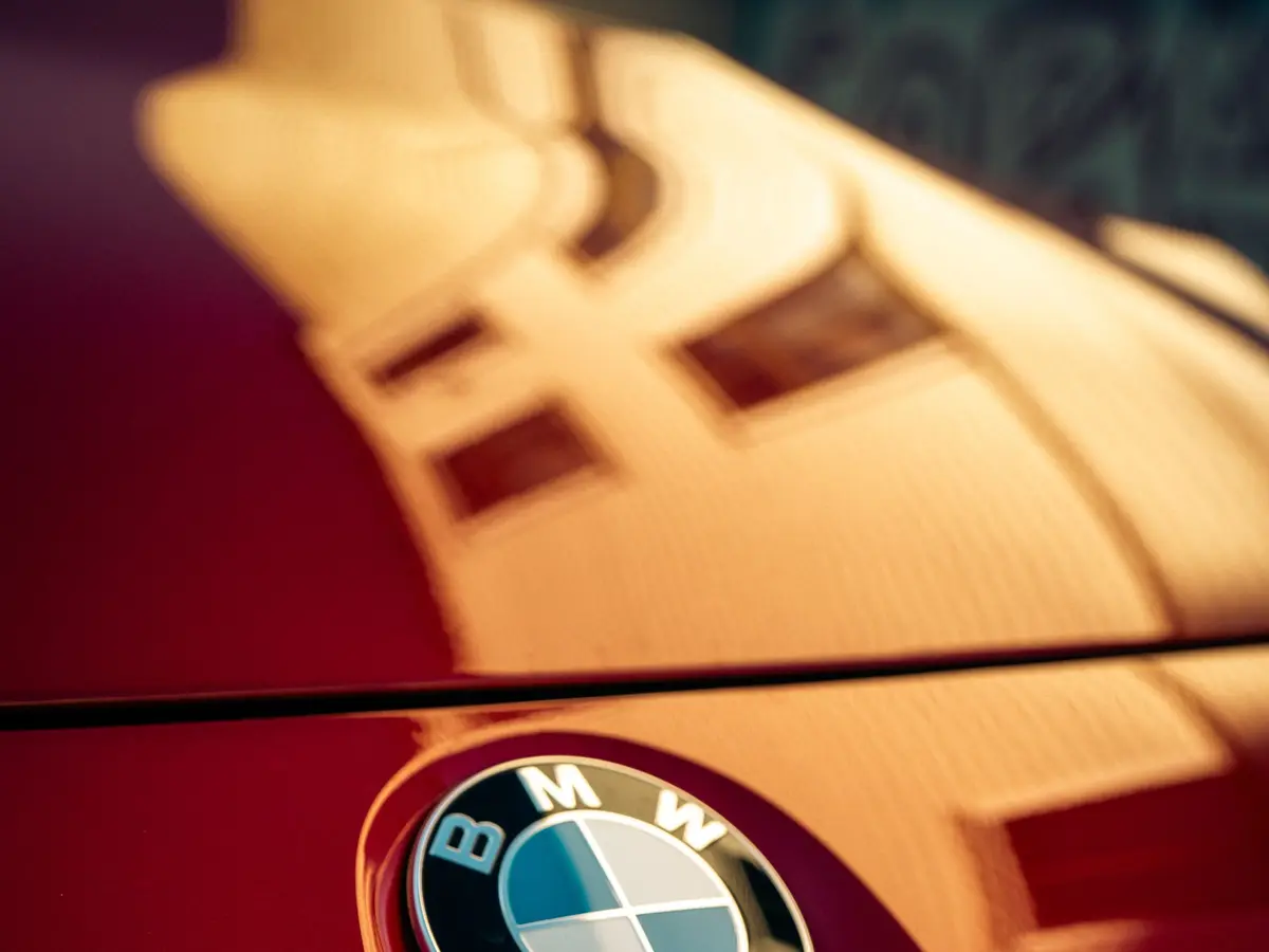 Červená kapota BMW se znakem, v laku se zrcadlí okna
