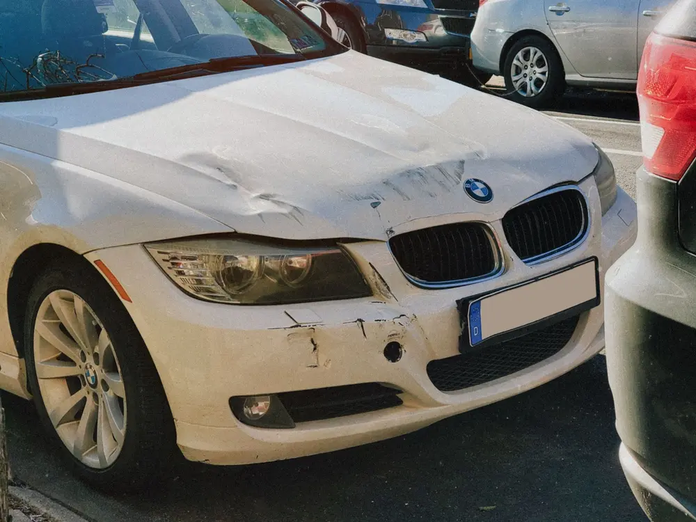 Bílé BMW s pomačkanou kapotou a nárazníkem po nehodě